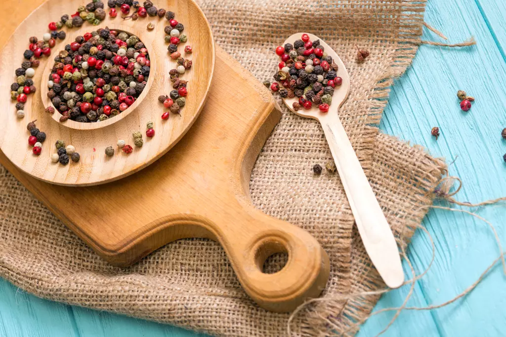 herbes-et-epices-melange-de-poivrons-dans-des-assiettes-en-bois-et-cuillere-sur-fond-bleu